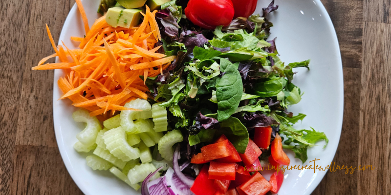 Plate of chopped vegetables, leafy greens, tomatoes, red peppers, celery, red onion, carrots, and avocado.