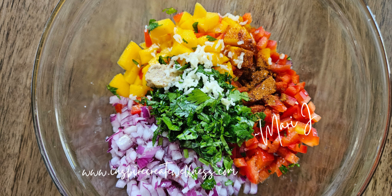 Chopped mango, red pepper, cilantro, red onion, garlic, and spices in a bowl.