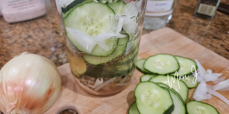 Sliced cucumbers in a jar with onions, garlic, and vinegar.