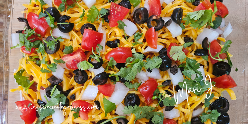 Chopped onions, cilantro, tomatoes, and olives on top of cheddar cheese bean dip