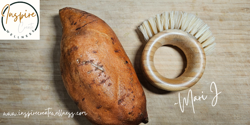 A clean sweet potato and a vegetable scrub brush on a cutting board