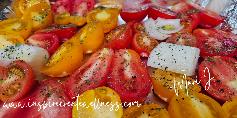 Sliced tomatoes, onions, and garlic on a baking sheet with olive oil and spices