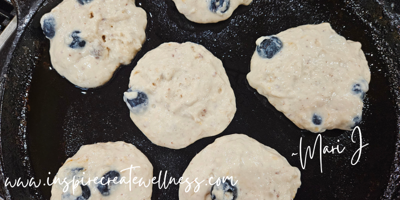 Blueberry Kefir Pancakes cooking on an iron skillet in coconut oil